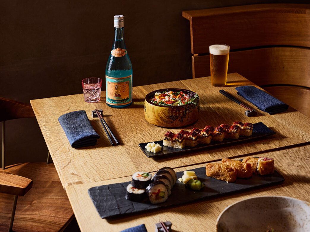 Ala carte menu items are displayed on a wooden table top at HIROKI, including a glass of beer, Futomaki, Hakuzushi and Niku Inari.