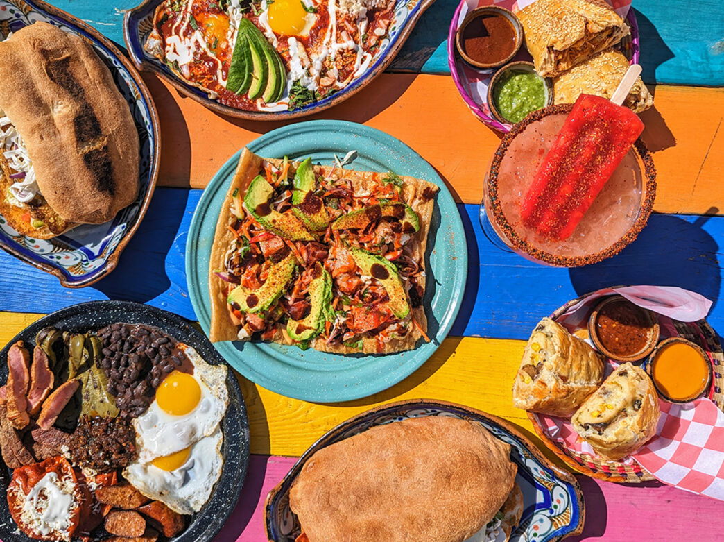 Various menu items are displayed on a picnic table painted with teal, orange, blue, yellow and pink paint at Cantina La Martina.