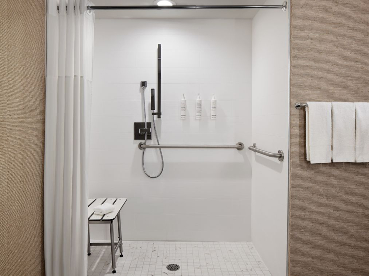 ADA compliant roll-in shower with white tile, a shower bench and grab rails.