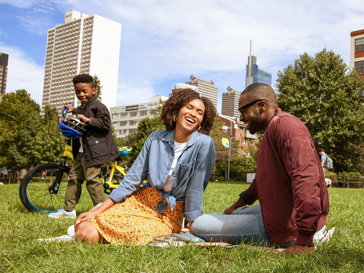 Family of three laughing on the grass of the Schuylkill Banks