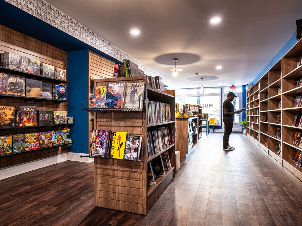 A person wearing a black shirt and dark jeans looks at a magazine while inside Multiverse in Philly. Various games, books, magazines and more are displayed on shelves throughout the store.