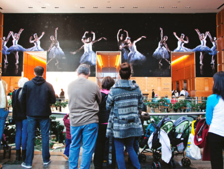 A crowd of onlookers watch as ballerinas from the Philadelphia Ballet, dressed in elegant white tutus, dance across the massive screen. The massive featuring a large screen displaying a dazzling ballet performance of dancers in elegant costumes.