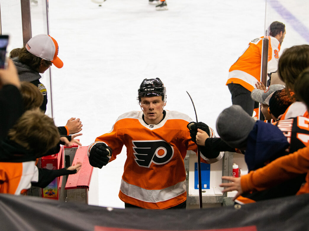 A Philadelphia Flyers player in an orange jersey high-fives fans as he heads off the ice.