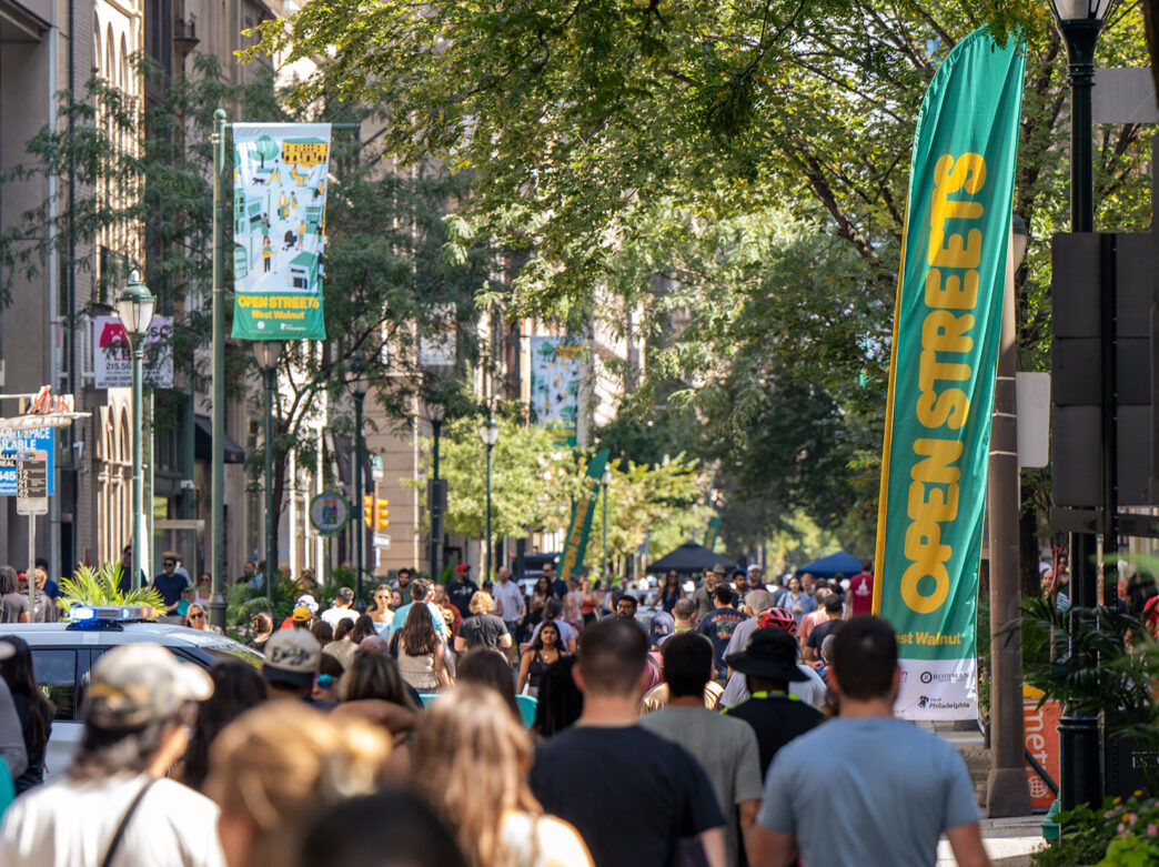 Crowds of people walk in a street closed to car traffic.