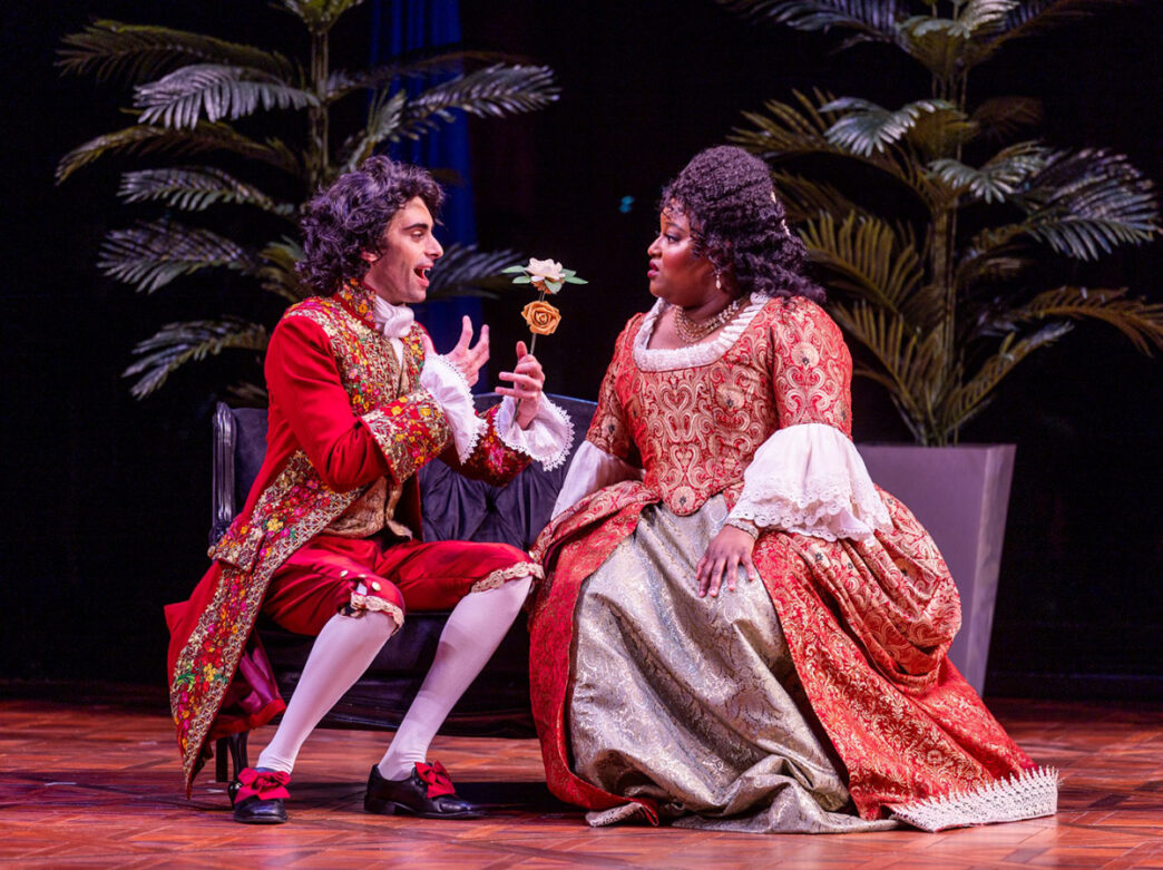 Two performers in elaborate period costumes share a heartfelt moment on stage during Opera Philadelphia's production of The Anonymous Lover.