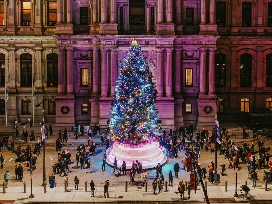 A large Christmas tree in front of City Hall is illuminated with colorful lights and decorated with ornaments.