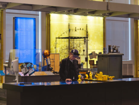 Een persoon kijkt naar een digitaal scherm bij een interactieve tentoonstelling in het Science History Museum. Op de achtergrond zijn gele en blauwe displays te zien.