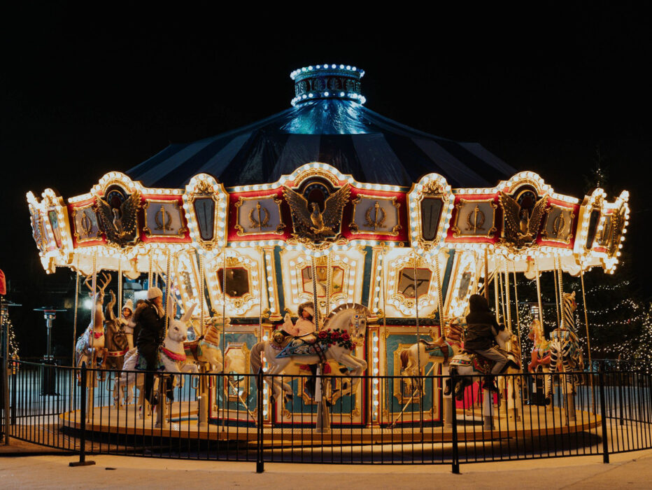 A carousel is lit up with bright lights against a dark sky while parents and children go for a ride at the Yuletide festival.