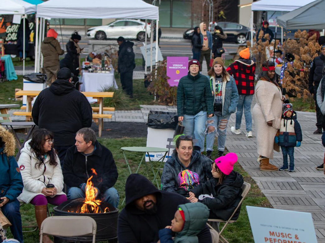 People sit around a bonfire and shop at vendor tens during the Holiday Fest at uCity Square.