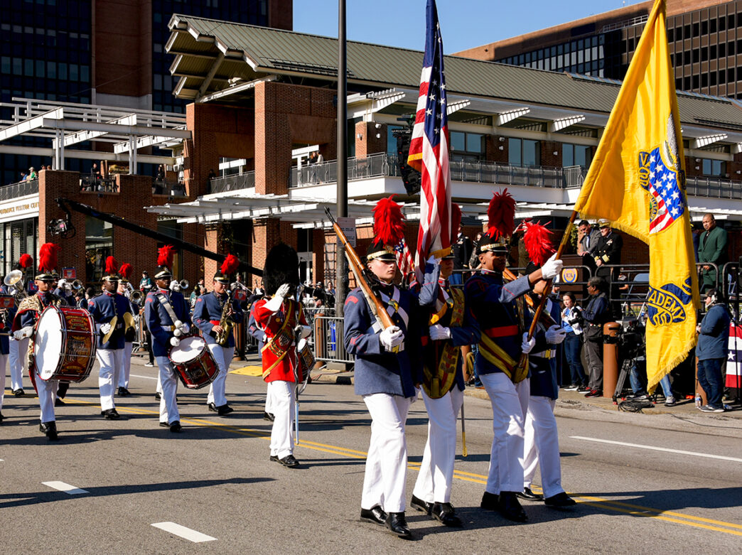 A marching band walks down the street during the Veterans Day Parade in Philadelphia. The band is lead by four men wearing military clothing and carrying flags.