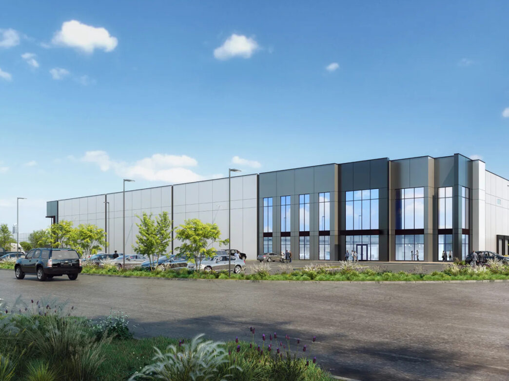 A rendering of a gray industrial building on the new The Bellwether District industrial campus. Cars are parked in a parking lot in front of the building.