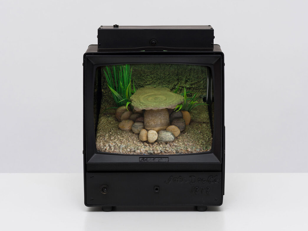 A piece of artwork by Carl Cheng for the Nature Never Loses exhibit at the Institute of Contemporary Art. The piece is a small box tv decorated with stones and grass.
