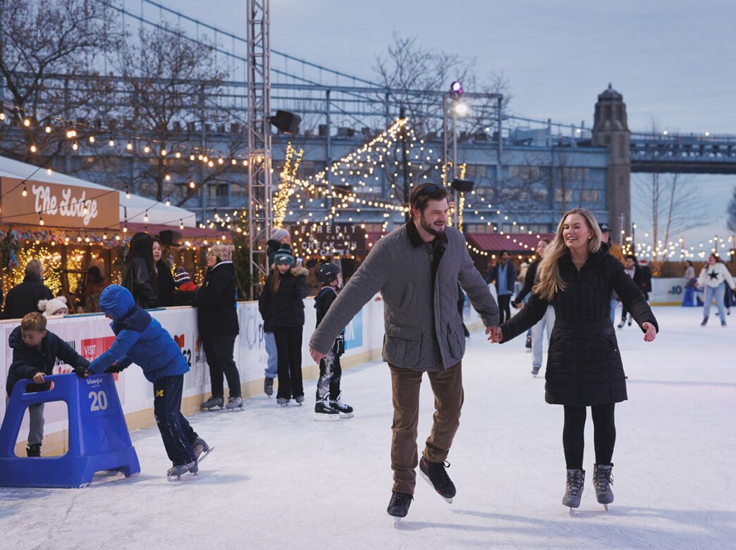 A couple, dressed warmly in winter coats, smile and skate across the Independence Blue Cross RiverRink.