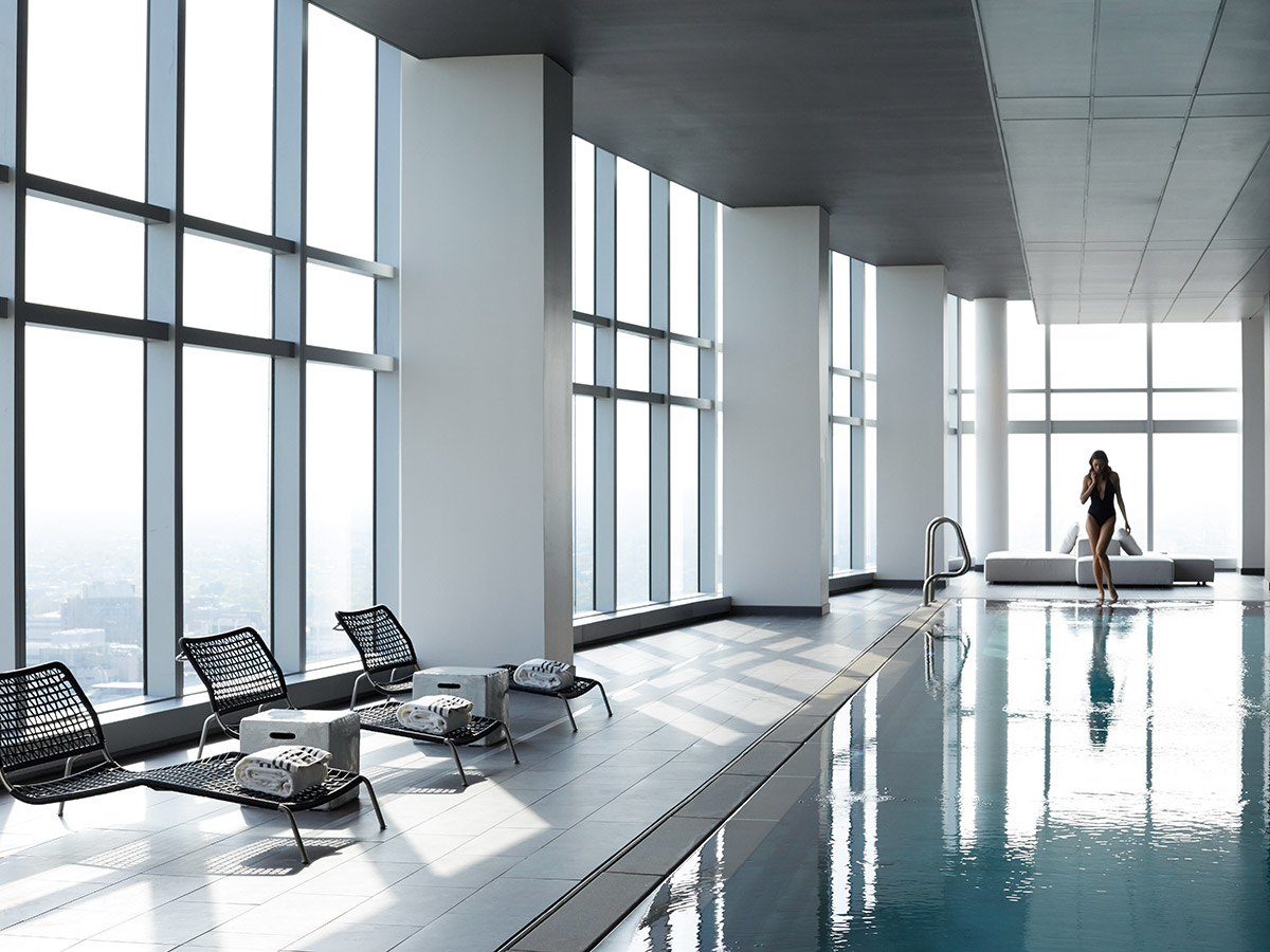A woman in a black swimsuit walks along the edge of the sleek pool at the AKA University City.