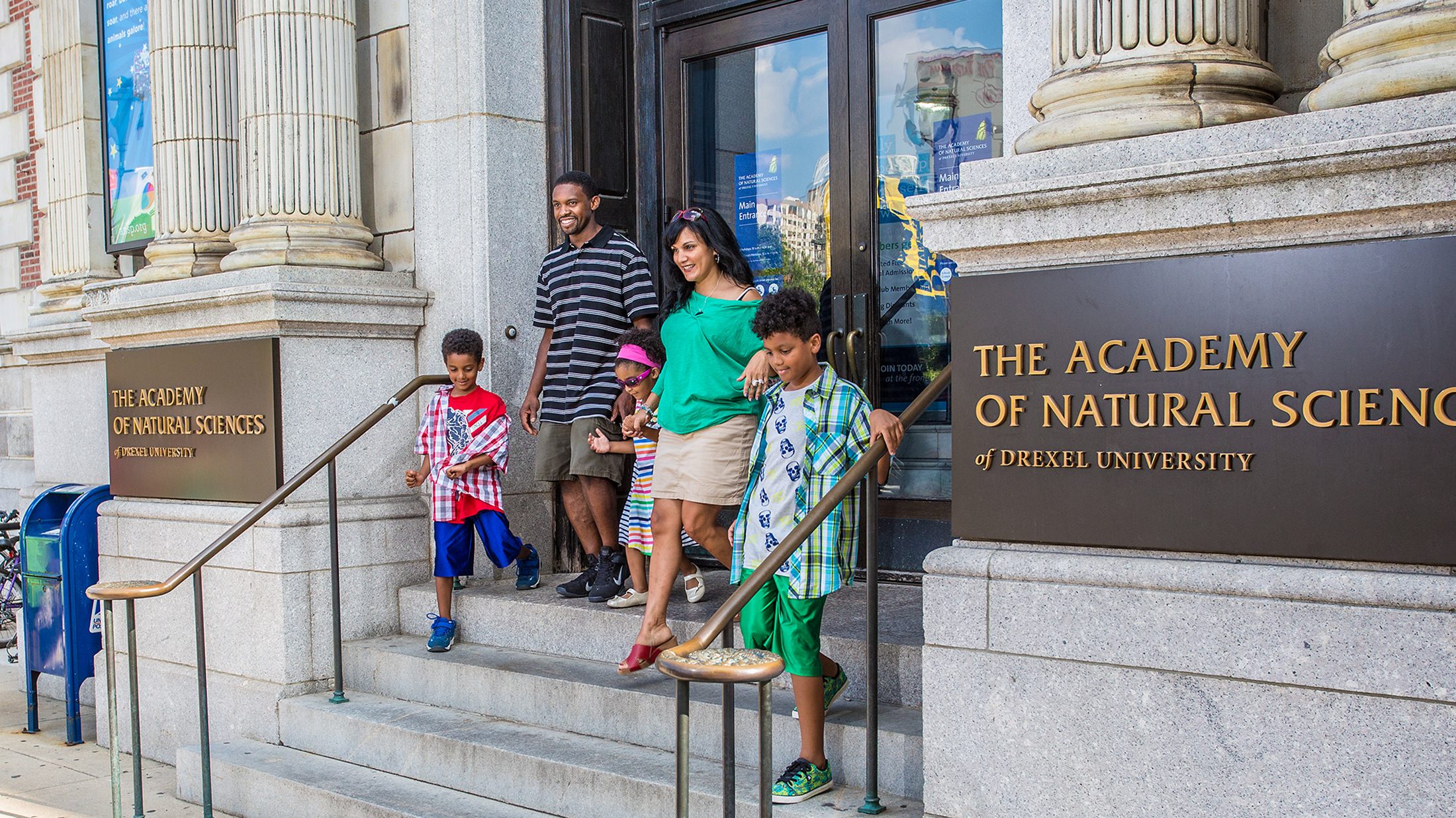A family of five walks down the granite steps out of The Academy of the Natural Sciences of Drexel University.