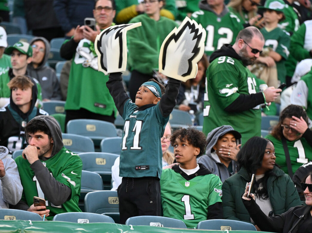 Een grote groep Eagles-fans op de tribune bij Lincoln Financial Field. Een jonge fan steekt zijn armen in de lucht.