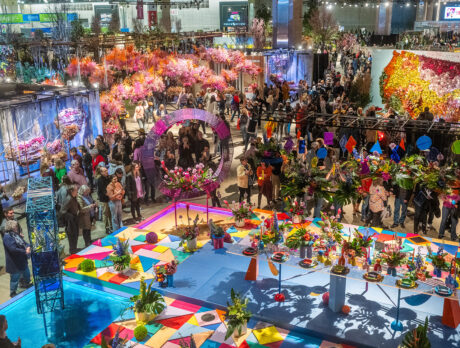 An aerial view of the Philadelphia Flower Show exhibit hall. People walk around and observe the colorful floral displays.