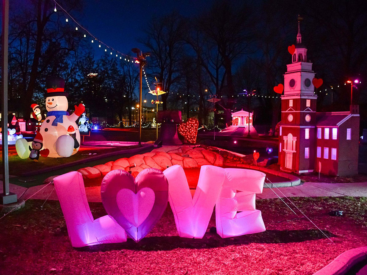 Uma cena no Chilly Philly Mini Golf apresenta luzes coloridas vibrantes, bonecos de neve infláveis, uma réplica do Independence Hall e uma exibição rosa brilhante com a palavra "LOVE" e um coração no centro.