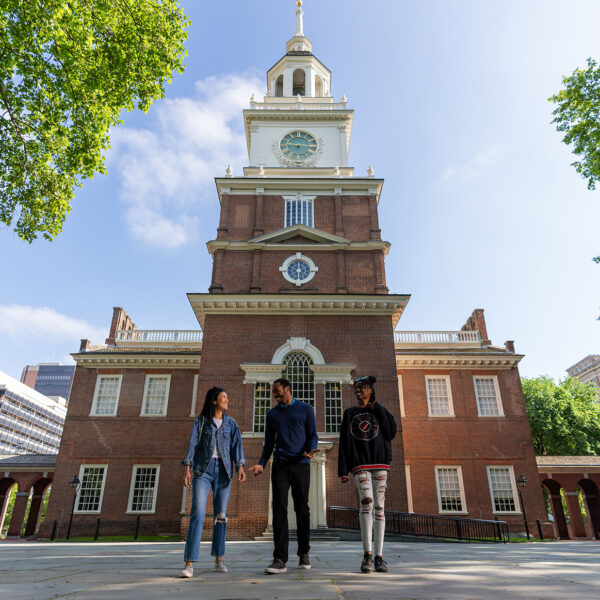 Three people walk with the back of Philadelphia's Independence Hall in the background.