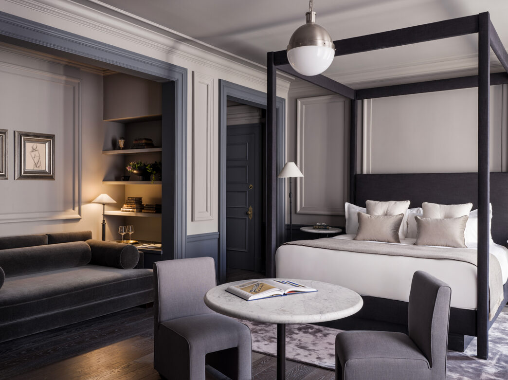 A black four poster bed, a cafe table and a lounge sofa furnish a Junior Suite at The Bellevue Hotel. The room is decorated with gray, tan and black hues.