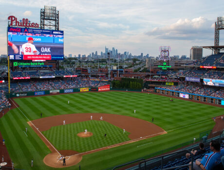 A panoramic view of the Phillies game at Citizens Bank Park showcases the vibrant green field, the towering scoreboard, and the Philadelphia skyline in the distance.