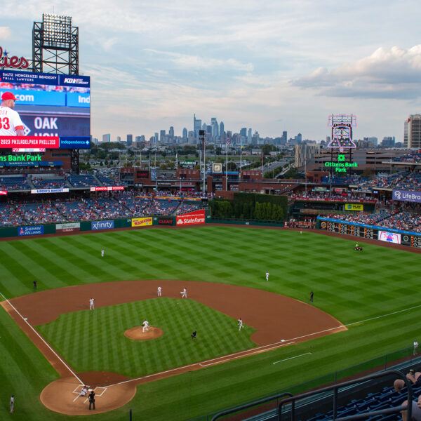 A panoramic view of the Phillies game at Citizens Bank Park showcases the vibrant green field, the towering scoreboard, and the Philadelphia skyline in the distance.