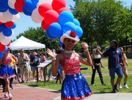 People walking in a parade line holding colorful balloons during Red, White & Blue To-Do. A woman waves at the camera