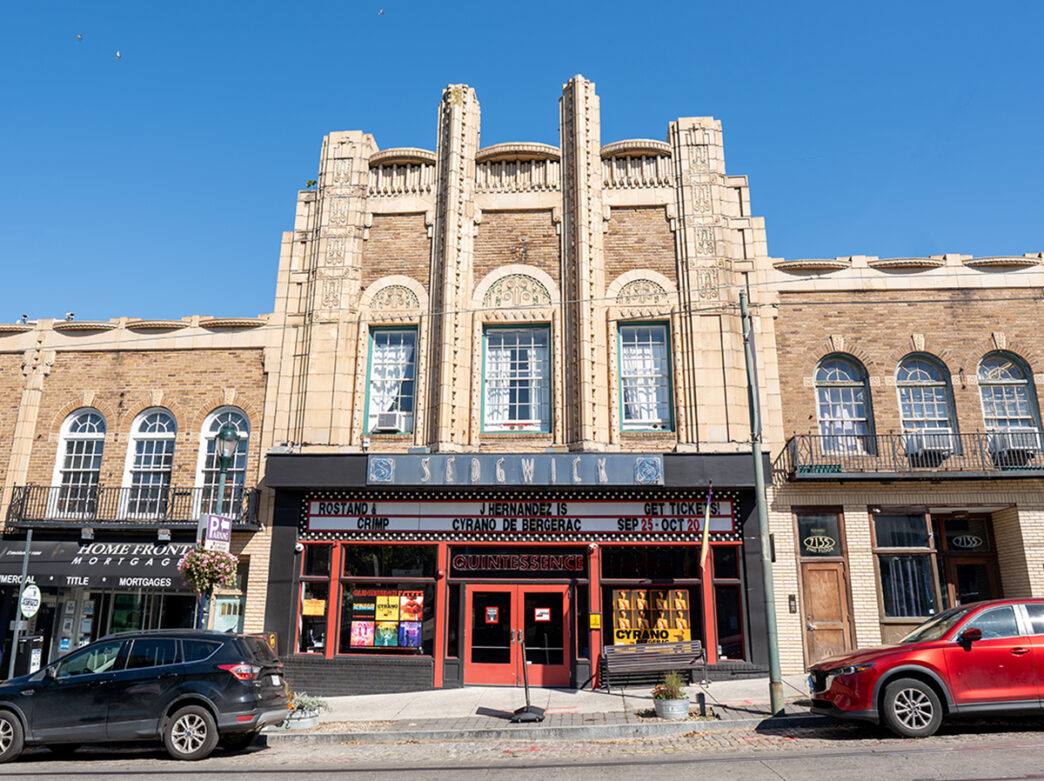 The exterior of a tan brick building with a theater awning and marquee sign.