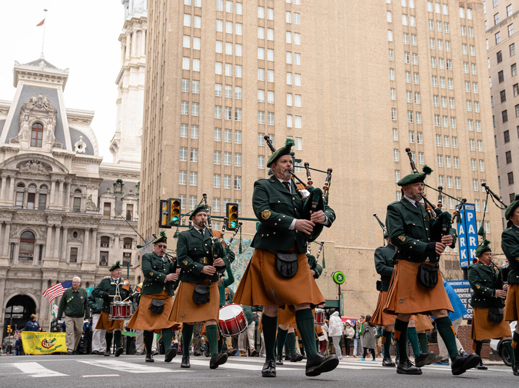 Bagpipers wearing green coats and brown kilts march down Broad Street while playing the bagpipes for the St. Patrick's Day Parade in Philadelphia.