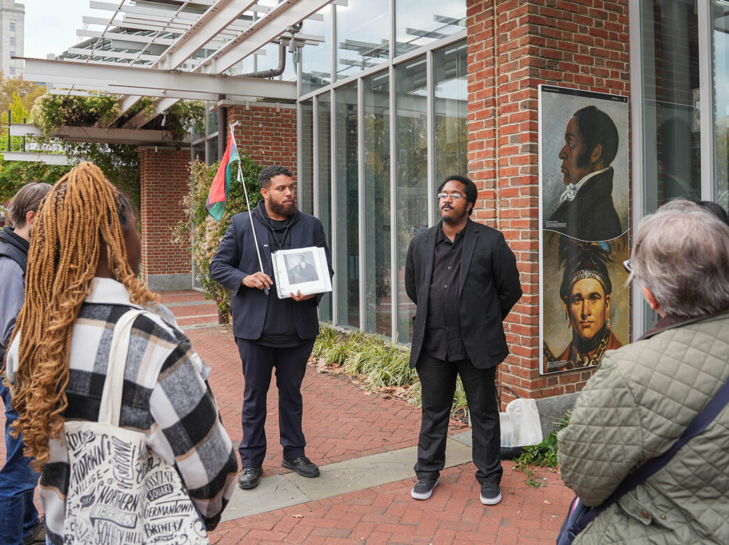 Tour tour guides wearing all black lead a group in the The Original Black History Tour in Philadelphia. The group stops in front of the Liberty Bell Center.