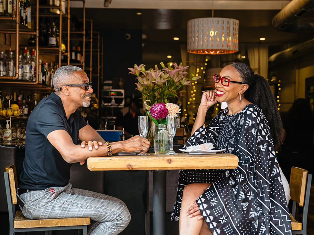 A couple sit across from each other while sitting at a table in Booker’s Restaurant & Bar. There are champagne glasses and a small bouquet of flowers on the table.