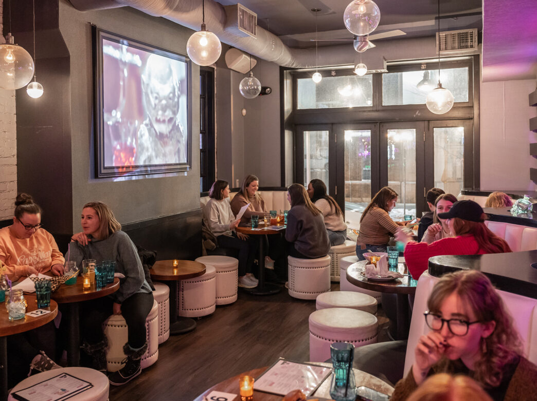 People in booths and on stools while dining at Monster Vegan in Philadelphia. Drinks, food and menus are on the tabletops.