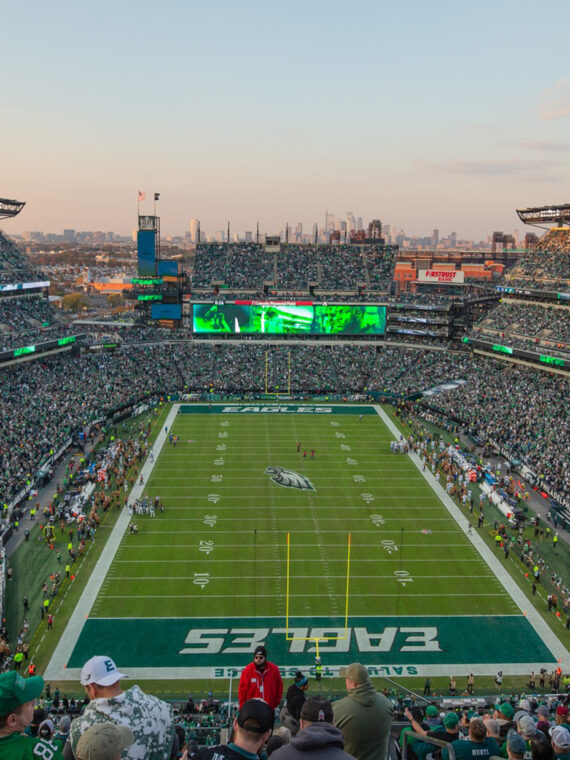 A packed Lincoln Financial Field during a Philadelphia Eagles game, with fans filling the stands around the football field and the Philadelphia skyline visible in the distance.