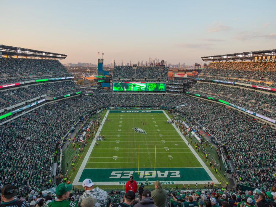 A packed Lincoln Financial Field during a Philadelphia Eagles game, with fans filling the stands around the football field and the Philadelphia skyline visible in the distance.