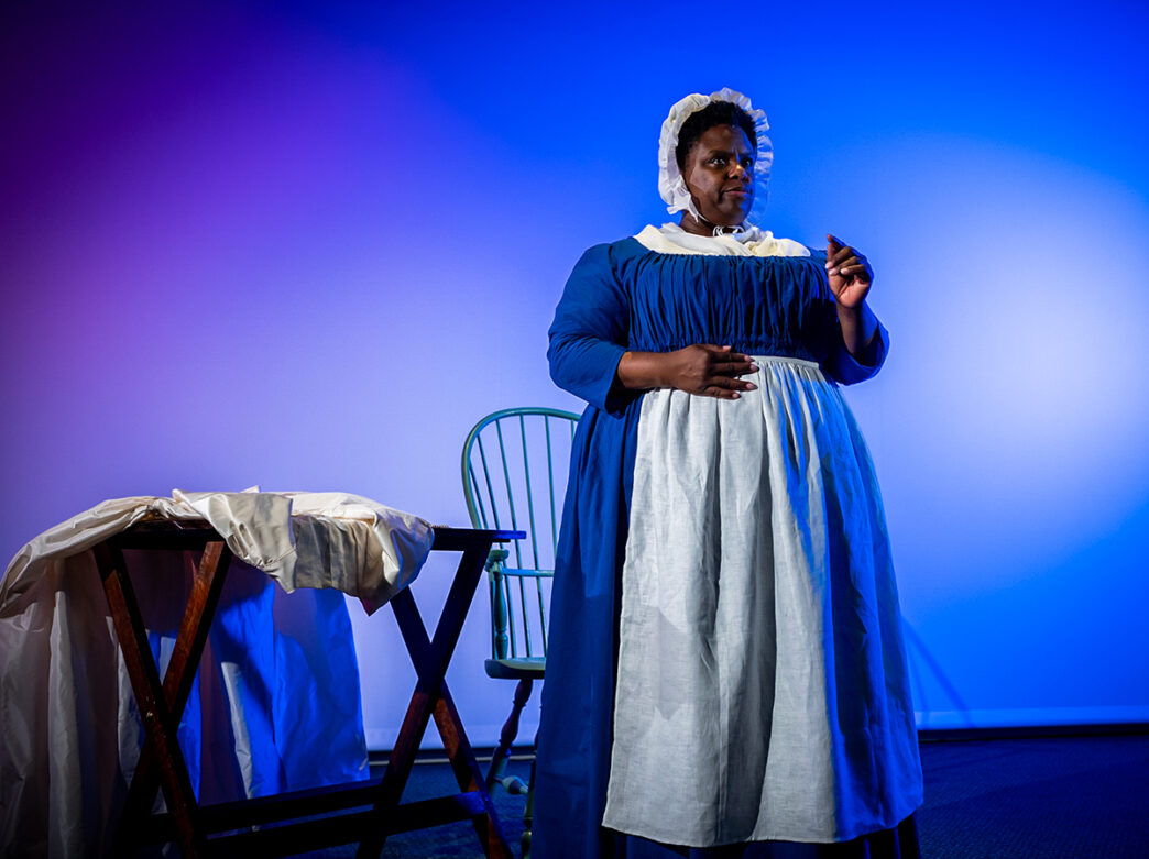 An actress portraying Elizabeth Freeman wears a blue dress, white apron and white bonnet performs Meet Elizabeth Freeman at the Museum of the American Revolution.