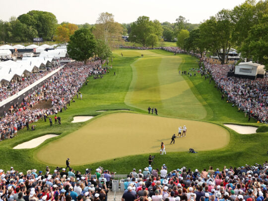 Crowds of spectators watch a professional golfer on the green and fairway during the PGA Championship.