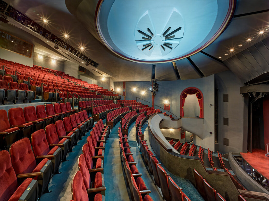 The interior of Walnut Street Theatre. Red velvet theater seats facing the stage fill the theater.