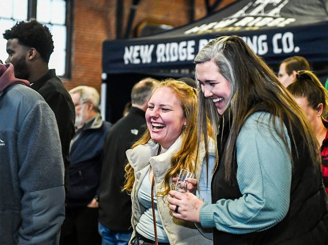 Two people holding beer samplers laugh while at the Philly Beer Fest at 23rd Street Armory.