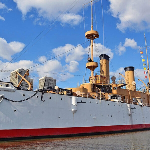 Photo of the USS Cruiser Olympia floating on the Delaware River, Philly skyline in the background