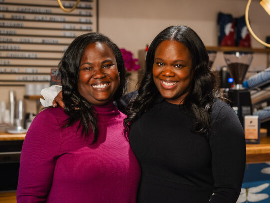 Sisters Sharaine and Sharla Brown pose for a photo and smile at the camera together at their coffee shop Arterial Coffee.