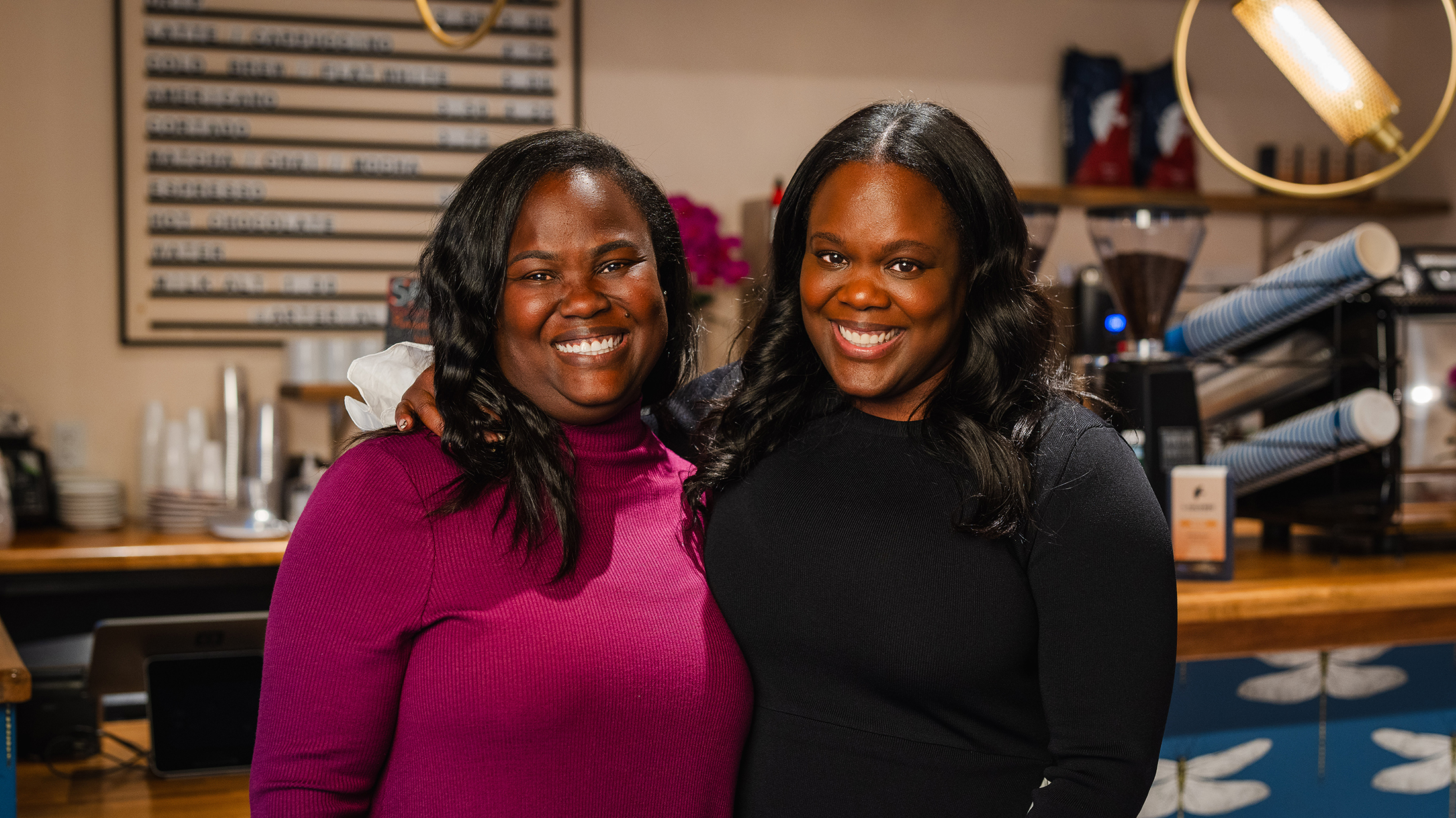 Sisters Sharaine and Sharla Brown pose for a photo and smile at the camera together at their coffee shop Arterial Coffee.