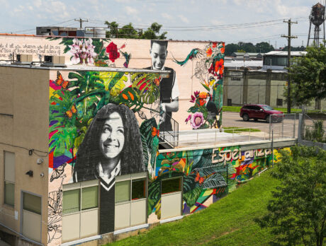 A vibrant mural on the side of a building in Philadelphia features large black-and-white portraits of two young individuals surrounded by lush, colorful tropical plants, flowers, butterflies, and birds.