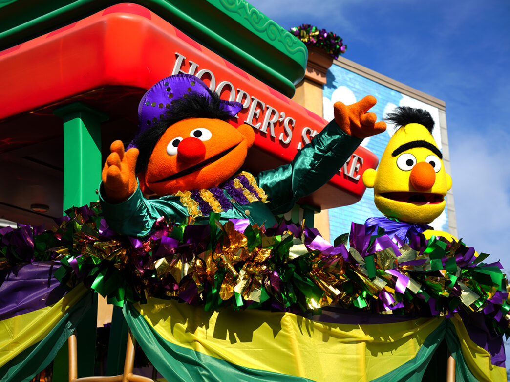 Sesame Street characters Bert & Ernie ride on a parade float decorated with purple and green foil streamers during the Sesame Place Mardi Gras Parade.
