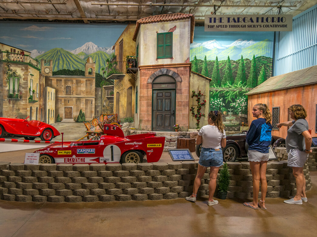 Three women examine a red race care on display at the Simeone Foundation Automotive Museum. One person points to a car.