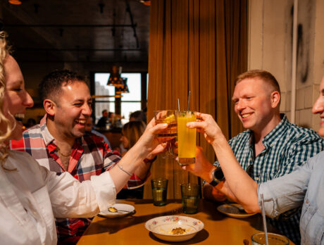 A group of four friends at a collaborative dinner at Irwin's toast their cocktails.
