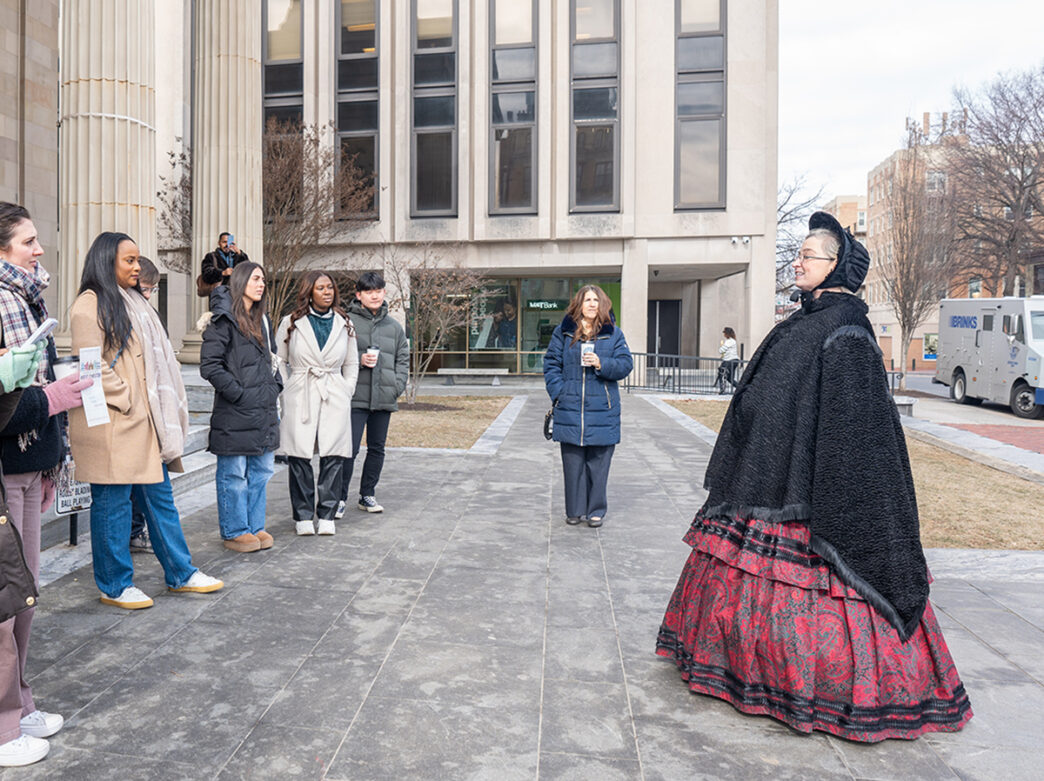 A woman dressed in historical clothing faces a tour group while leading a history tour in West Chester.