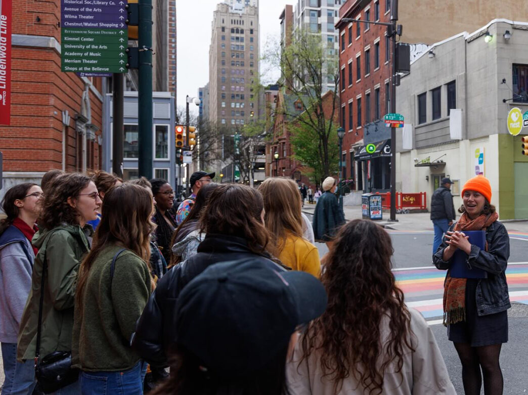 A group of college students face a tour leader wearing an orange beanie while attending a tour of Philadelphia from Beyond the Bell Tours.