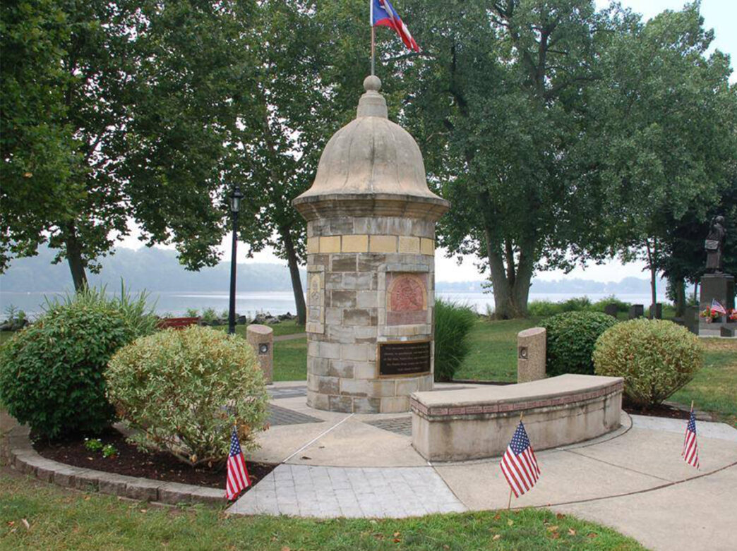 A stone monument sits in a park overlooking the Delaware River in Bristol, PA. The monument is a replica of a guard house of El Morro dedicated to Puerto Ricans.