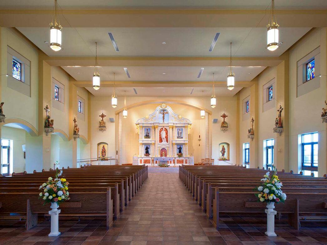 The interior of St. Rocco Catholic Church. Pews face an intricately decorated alter with statues and a cross.