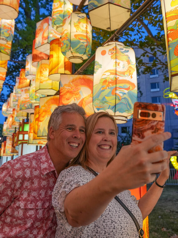 Two people pose for a selfie while walking through a walkway illuminated by Chinese lanterns at the Chinese Lantern Festival in Philadelphia.